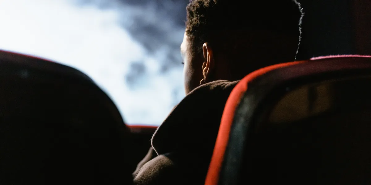 A person seen from behind in a dark cinema, silhouetted against the bright screen with red-piped seats on either side